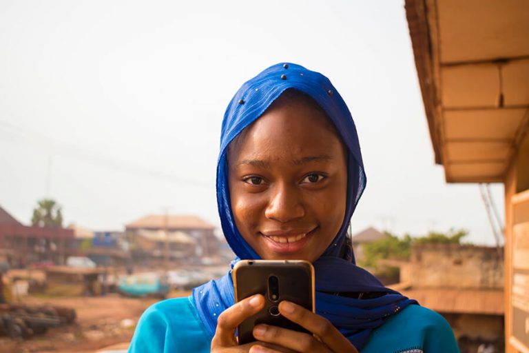 An African woman on her phone, smiling at the camera