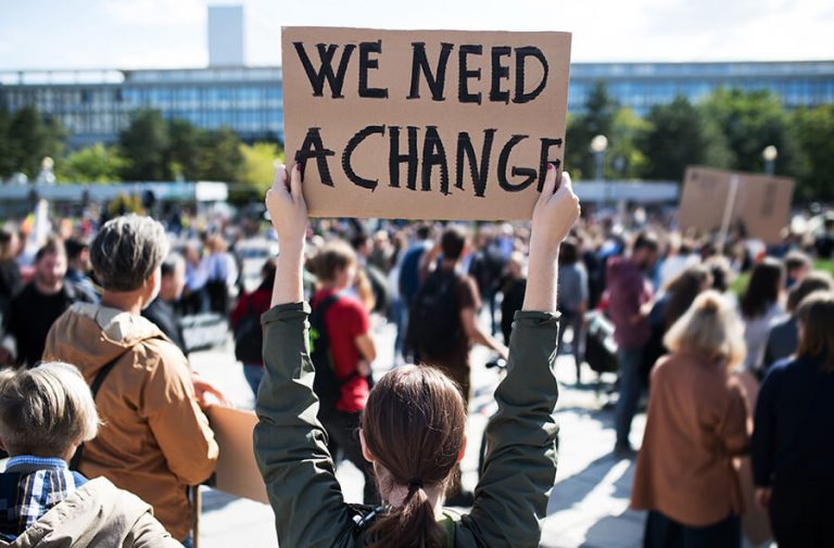 A group of protestors holding up a cardboard sign that reads "We need a change"